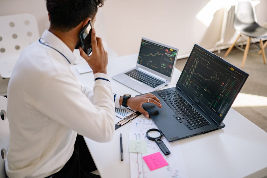 Man working on multiple laptops with financial charts visible on screens at a desk